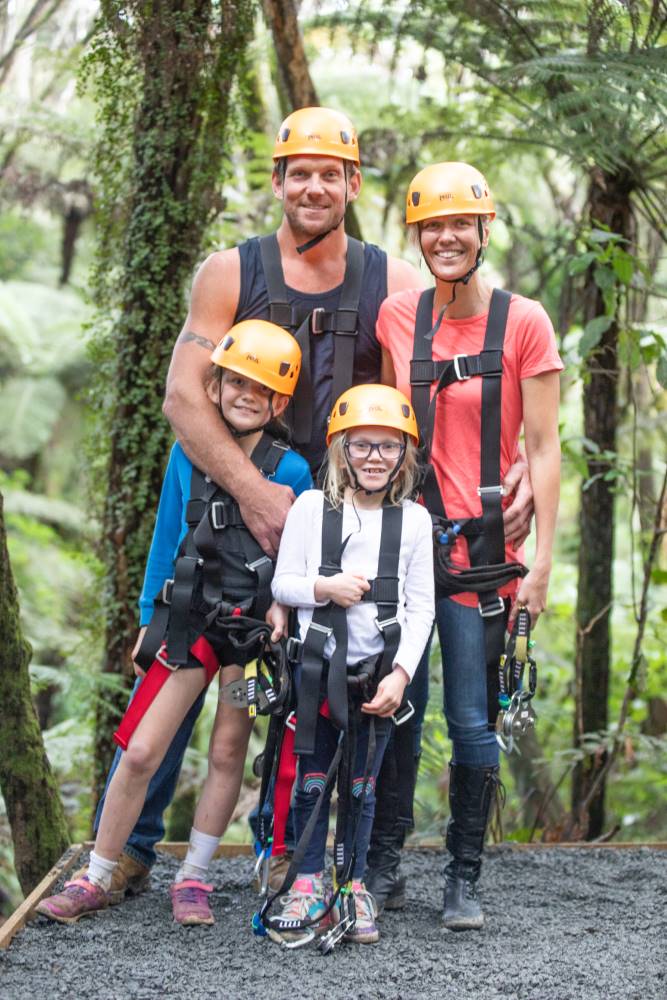 Family in helmets and harnesses ready for the zipline among tall trees.